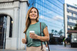 © Jelena Stanojkovic - Beautiful woman going to work with coffee walking near office building. Portrait of successful business woman holding cup of hot drink in hand on her way to work on city street.
