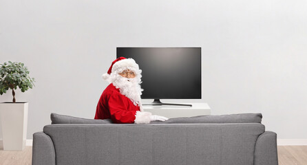 Santa claus resting on a sofa in front of tv and looking at camera