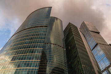 Angled view of modern skyscrapers in business district against blue sky. Looking Up high-rise office buildings. Evening time, sunset. Orange, yellow and gold shades of color.