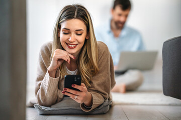 Wall Mural - Smiling young woman chatting in social networks, working, using mobile applications at home.