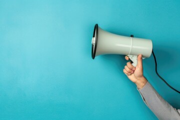 A person holds a megaphone in front of a bright blue wall, perfect for public speaking or protest demonstrations