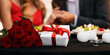 © Prostock-studio - Romantic Couple Holding Hands, Celebrating Valentine's Day In Restaurant With Present Box And Red Roses Bouquet Lying On Table In Foreground, Closeup