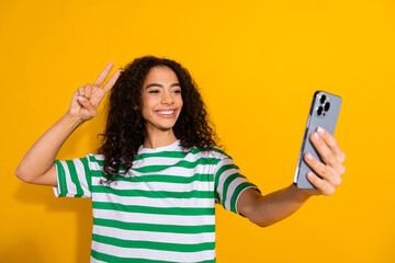 photo of pretty young girl phone selfie v-sign wear striped t-shirt isolated on yellow color backgro