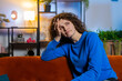 © Andrii Iemelianenko - Portrait of upset lonely young woman with curly hair thinking about problems sitting on sofa in living room at home. Bored female girl feeling bad annoyed burnout while looking away in apartment