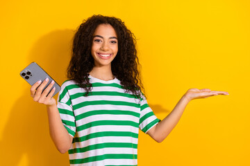 Wall Mural - Portrait of nice young girl hold phone empty space wear striped t-shirt isolated on yellow color background