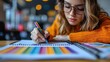 © NOPPHINAN - Young woman with glasses drawing colorful patterns in notebook, focusing on creative work. Casual indoor setting with blurred background.