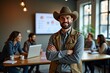 © Mediaphotos - Smiling man wearing cowboy hat standing with arms crossed in modern office with team members collaborating in background, brightly lit and productive setting