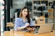 © Nuttapong punna - Young Asian woman, smiling and working at her desk in an office environment.