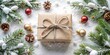 © VisualVault - A rustic brown gift box adorned with twine bow, resting on a snowy surface amidst evergreen branches and festive ornaments.