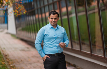 Portrait of a happy young businessman standing near the modern office building. A handsome confident young man standing and smiling in a blue shirt outside.