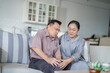 © ultramansk - An elderly couple sits in their living room. The man holds his knee, appearing to be in discomfort, while his partner offers support. The image conveys care, concern, and the bond between the couple.