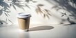 © VisualVault - A single takeaway coffee cup with a white lid sits on a white surface with a shadow cast by the light shining through a nearby window, creating patterns of foliage.