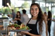 © Milos - In a busy school cafeteria, a smiling teenage girl serves a fresh salad, showcasing hospitality and positivity, amidst a bustling backdrop of students and trays.