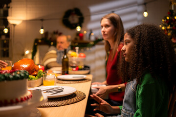 Grandfather, parents, and the teenage girls are all having dinner together at home on Christmas night