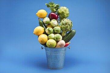 Poster - Assorted fresh fruits and vegetables in a metal bucket against a blue background