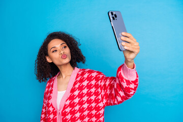 Wall Mural - Portrait of american beautiful girl with curly hair wearing red stylish cardigan photographing selfie kisses isolated on blue color background