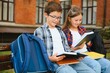 © Serhii - Children read books sitting on bench in school yard. Back to school. Beginning of school lessons