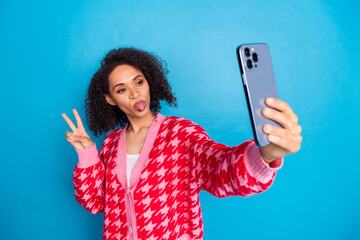 Wall Mural - Portrait photo of american beautiful girl with curly hair stick out tongue photographing v sign isolated on blue color background