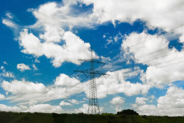 A tall high-voltage pole, a structure with high-power electric voltage, stands in a field against the sky.