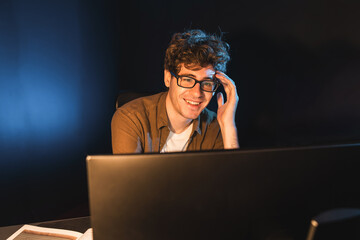 Smiling young businessman focusing on pc for creative startup project job at neon light modern office. Thinking marketing network online planning of creator to market channel design concept. Gusher.