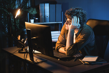 Stressful creative manager searching design thinking with new presentation while waiting email sending back on laptop screen at home office in casual shirt at neon light room at night time. Gusher.