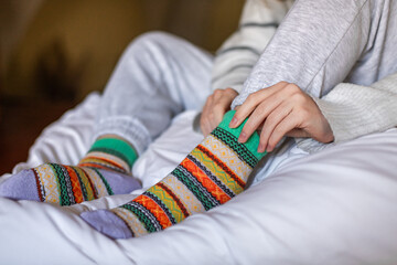 A woman in warm pants putting on a second pair of warm socks to keep warm in the winter without heating, energy and economic crisis concept