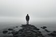 © Jahan Mirovi - A solitary person gazes across a serene fog covered lake surrounded by stillness on a rocky pathway leading into the water
