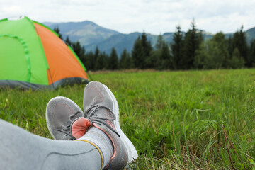 Canvas Print - Woman wearing trekking shoes and lying near tent outdoors, closeup. Space for text