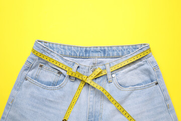 Sticker - Jeans and measuring tape on yellow background, top view