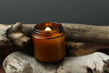 Poster - Beautiful burning candle on pieces of decorative wood against gray background, closeup