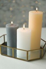 Canvas Print - Beautiful burning candles on white table against blurred lights, closeup