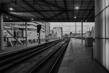 Black and white of a modern train station platform with tracks leading into the distance