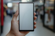 © Pixel World Vision  - A hand holding a blank smartphone display in a busy indoor shopping area during the daytime