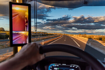 Wall Mural - View from the driver's seat of a truck on a highway with a dramatic sky, with the sunrise on the rearview mirror screen.