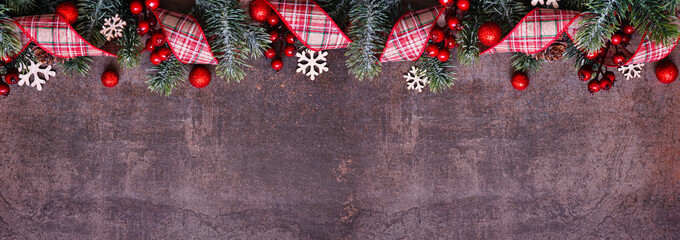 Wall Mural - Christmas top border of red plaid ribbon, baubles, snowflakes and frosty branches. Above view on a dark brown banner background. Copy space.