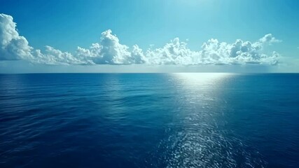 A clear blue sky with fluffy clouds above an expanse of deep blue ocean