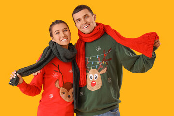 Poster - Young couple in Christmas sweaters with scarves on yellow background