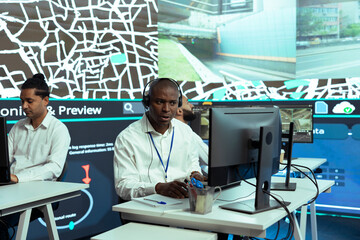 African american man offers updates to clients via order tracking service, monitoring delivery trucks through city traffic and providing gps coordinates. Dispatch employee in control center.