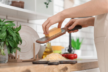 Young woman grating cheese on wooden cutting board in kitchen