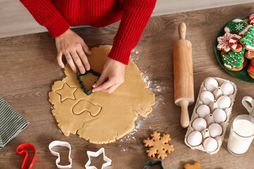 Wall Mural - Young woman with cutter making Christmas gingerbread cookies on table, top view