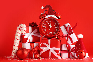 alarm clock with gift boxes and christmas decor on red background
