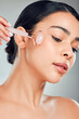 © KayExam/peopleimages.com - Skincare, woman and rose quartz roller for beauty, glow and circulation treatment. Face, stone and model with cosmetics for facial massage, wellness benefits and dermatology on gray studio background