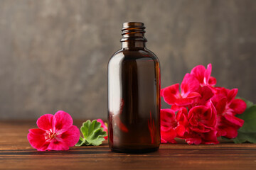 Poster - Geranium essential oil in bottle and beautiful flowers on wooden table