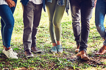 Group, legs and walking with friends on grass in park together for bonding, getaway or reunion. Fashion, footwear and jeans with shoes of people outdoor on lawn for holiday, travel or vacation