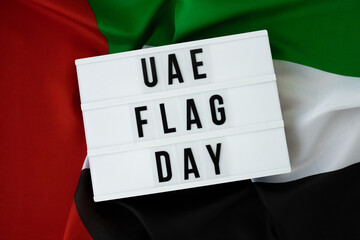 Lightbox with text UAE FLAG DAY on United Arab Emirates waving flag made from silk material. Independence Commemoration Day Muslim Public holiday celebration background. The National Flag of UAE