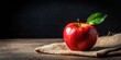 © Pluto - A Vibrant Red Apple Resting on Rustic Burlap Fabric with a Single Green Leaf on a Weathered Wooden Surface