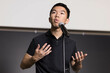 © fotolite - A young man confidently speaks to an audience in front of a microphone