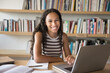 © fizkes - Happy beautiful smart African teenager girl enjoying being college student, sitting at table with books and laptop in university public library, looking at camera for portrait, smiling, laughing