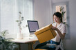 © PaeGAG - Young asian woman working in her home office is opening a parcel. She is sitting at her desk and holding a cardboard box