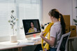 © PaeGAG - Young asian woman is holding a yellow sweater during a video call with a fashion blogger, discussing fashion trends and seeking advice on clothing choices